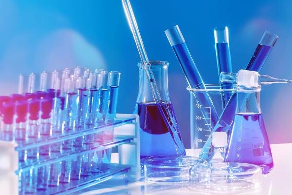 Two beakers and a tray of test tubes. Both the beakers and test tubes are filled with blue fluids and the image has blue lighting and background.